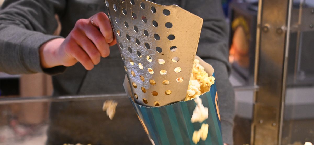 A woman scoops fresh popcorn into a green and blue popcorn bag.