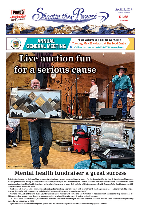 Smiling man with moustache grins as he shows a piece of art featuring mountains, while an auctioneer in blue shirt and cowboy hat calls the sale