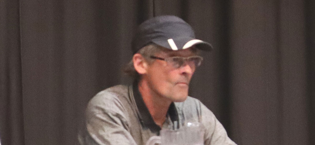 Independent candidate Erik Abildgaard – white male with grey hair and glasses wearing a blue and white ball cap and grey shirt with black collar.