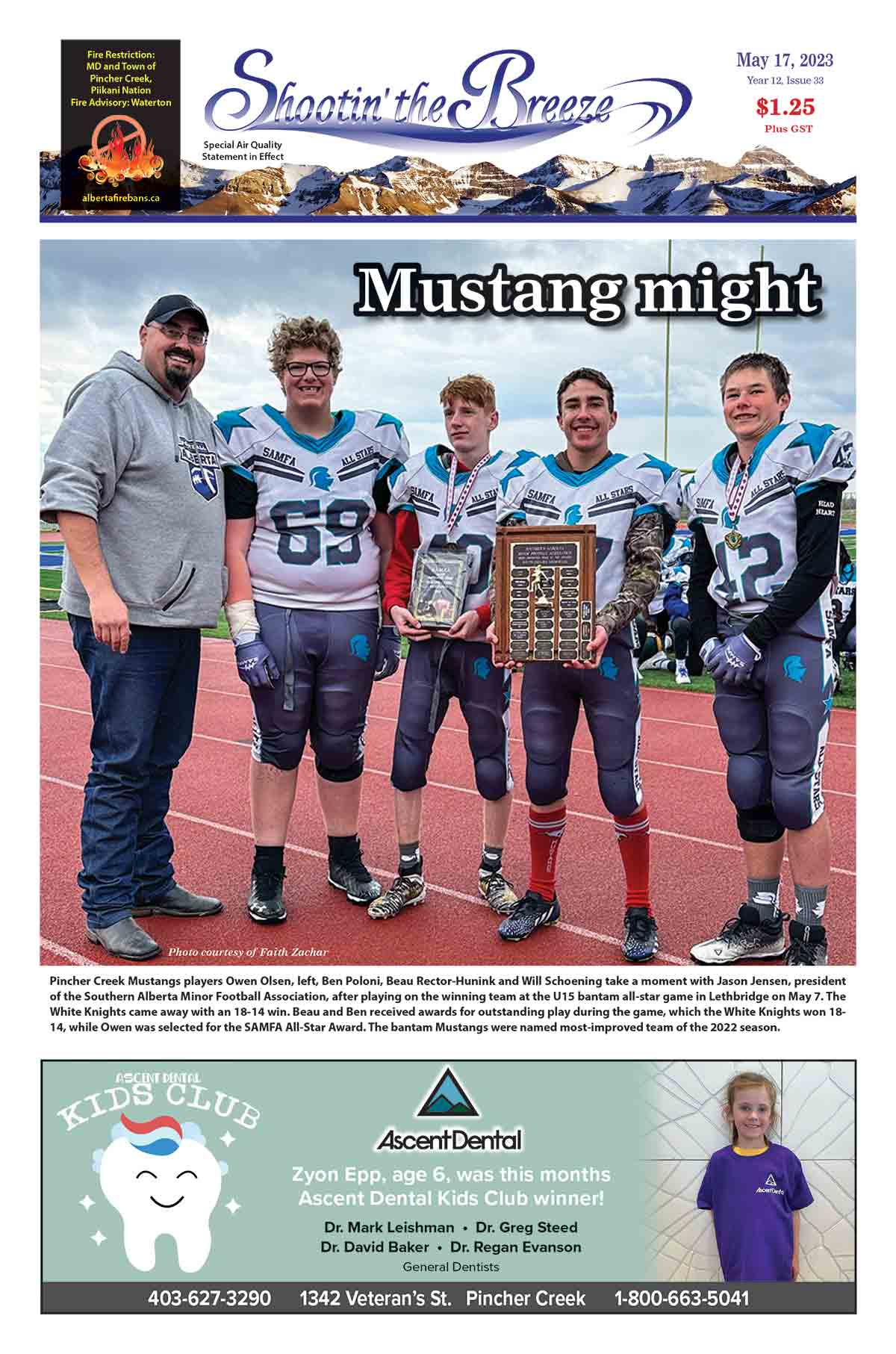 Four young male football players from the Pincher Creek Mustangs stand with a male coach.