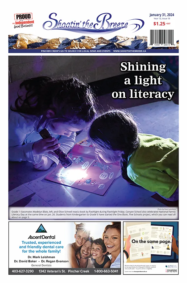 Two girls using a flashlight to read a book at Canyon School in Pincher Creek