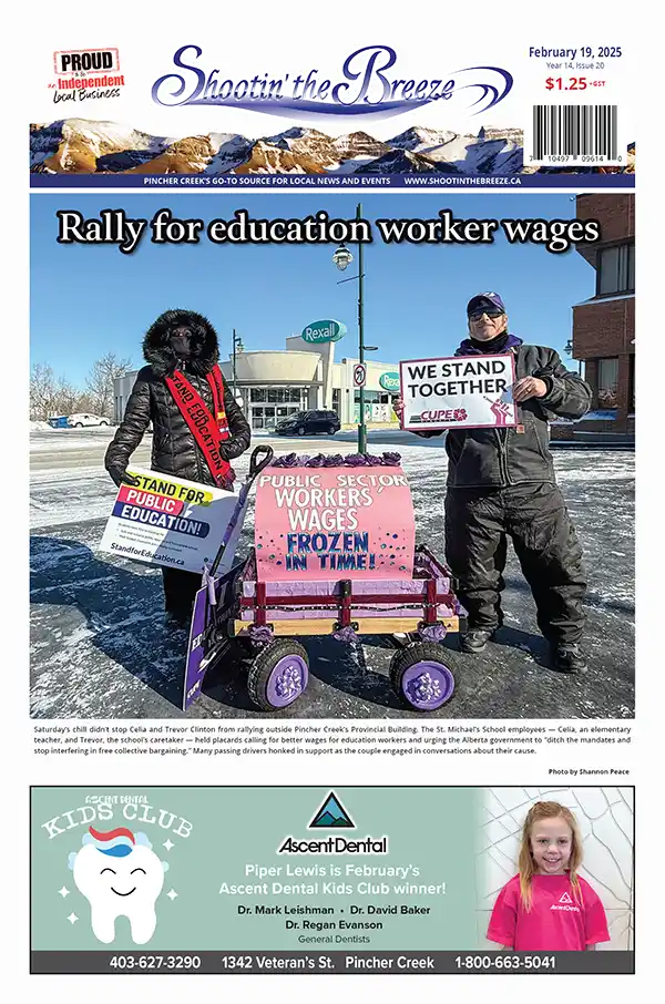 The front page of the Feb. 19, 2025, issue of Shootin' the Breeze features Trevor and Celia Clinton holding signs at a rally for education worker wages, one sign reads "We Stand Together," and another reads "Public Sector Workers Wages Frozen." A decorated wagon sits between them. It is cold and they are bundled up for the weather. Below is a promtion of Ascent Dental's Kids Club.