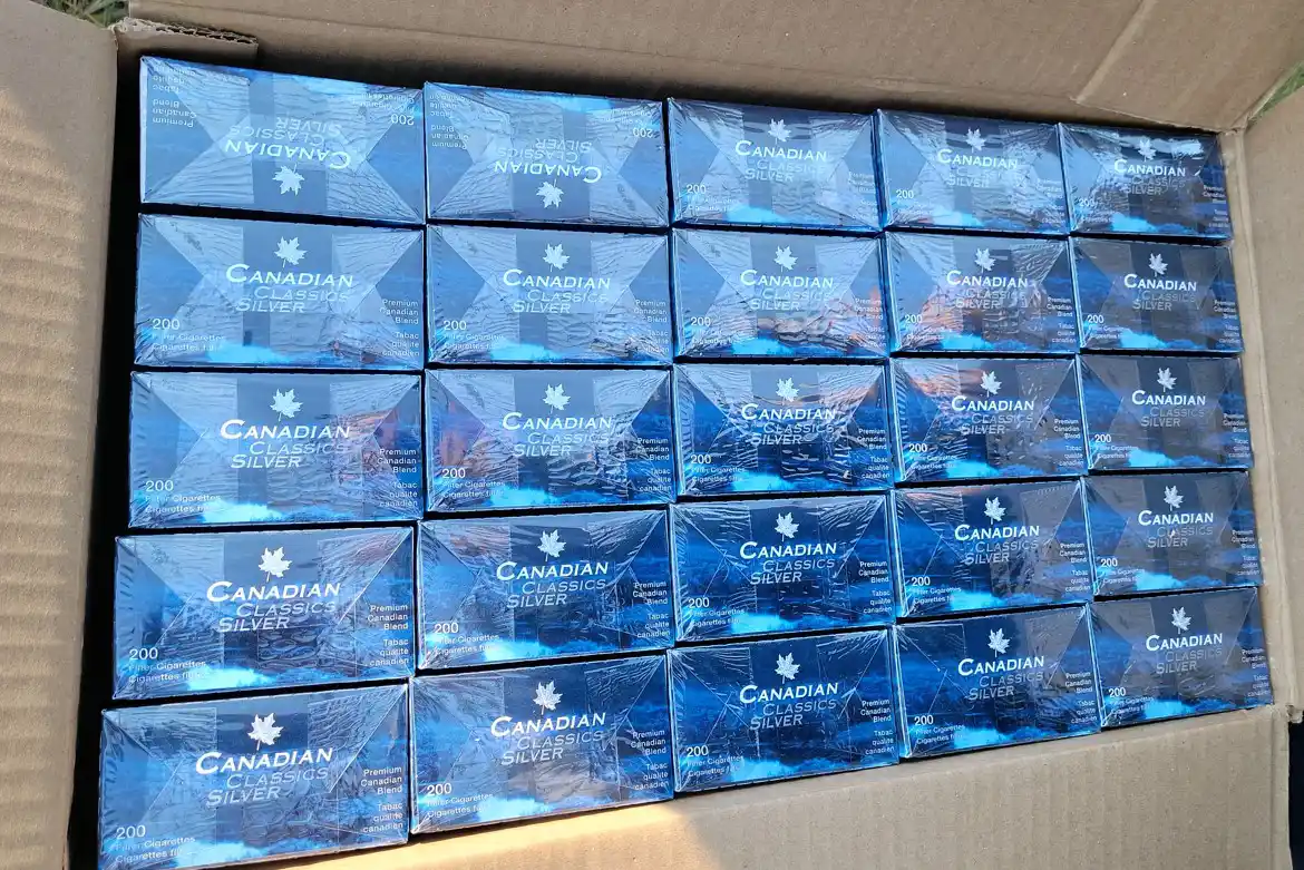 A cardboard box filled with multiple rows of blue cartons labeled "Canadian Classic Silver," each featuring a white maple leaf and text, all sealed in plastic.