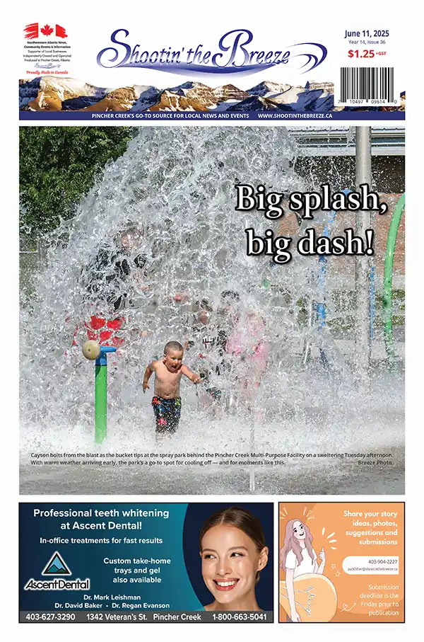 Two young children play and run through a large burst of water at a splash park on a sunny day. Water sprays up around them, creating a dramatic arc, while other children look on in the background.