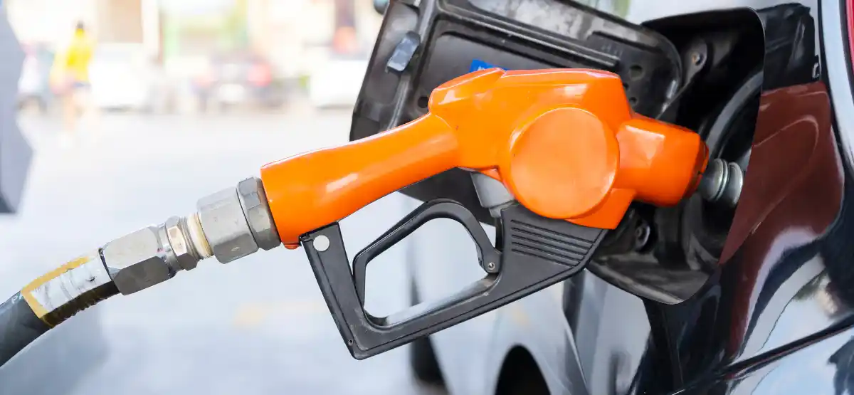 Close-up of an orange gasoline pump nozzle inserted into the fuel tank of a black vehicle at a gas station.