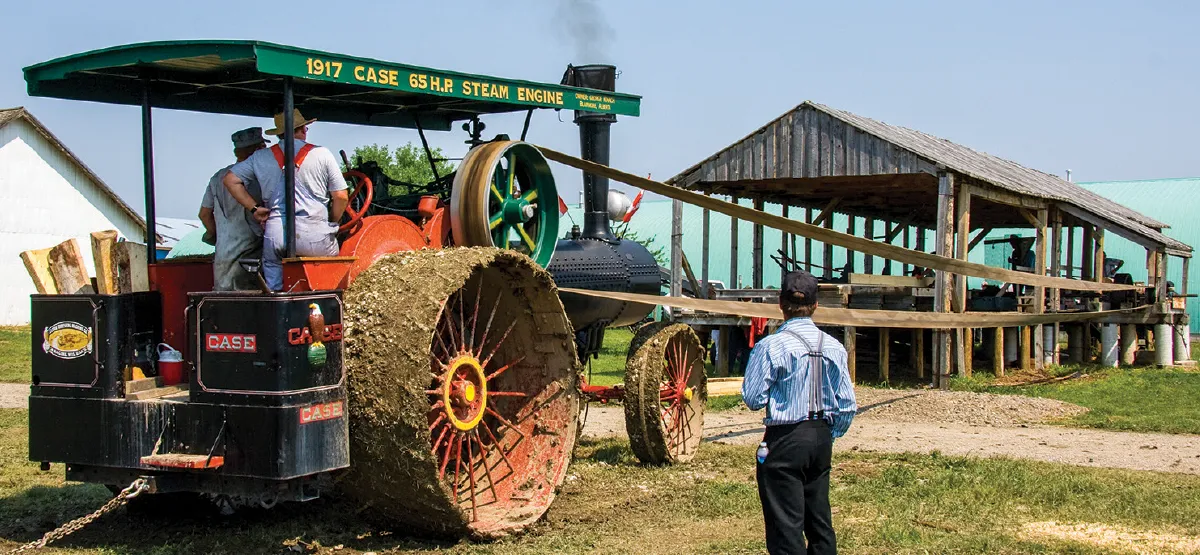 1917 Case steam engine tractor powering vintage sawmill at Heritage Acres with visitors watching