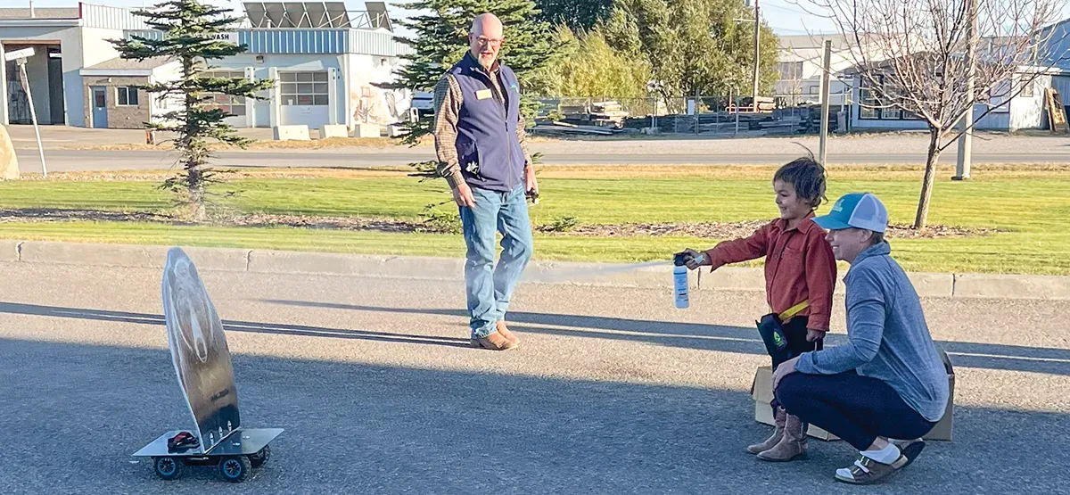 Man watches as young child with mother learns to use bear spray canister at outdoor safety workshop
