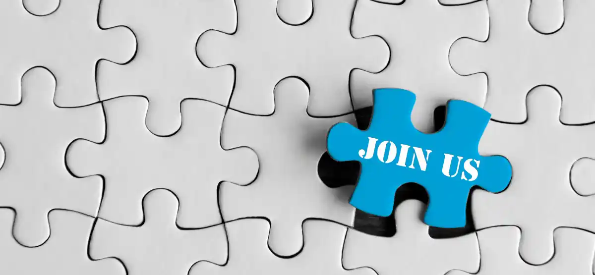 A blue puzzle piece with the words "JOIN US" written on it is about to be placed into a nearly completed white puzzle.